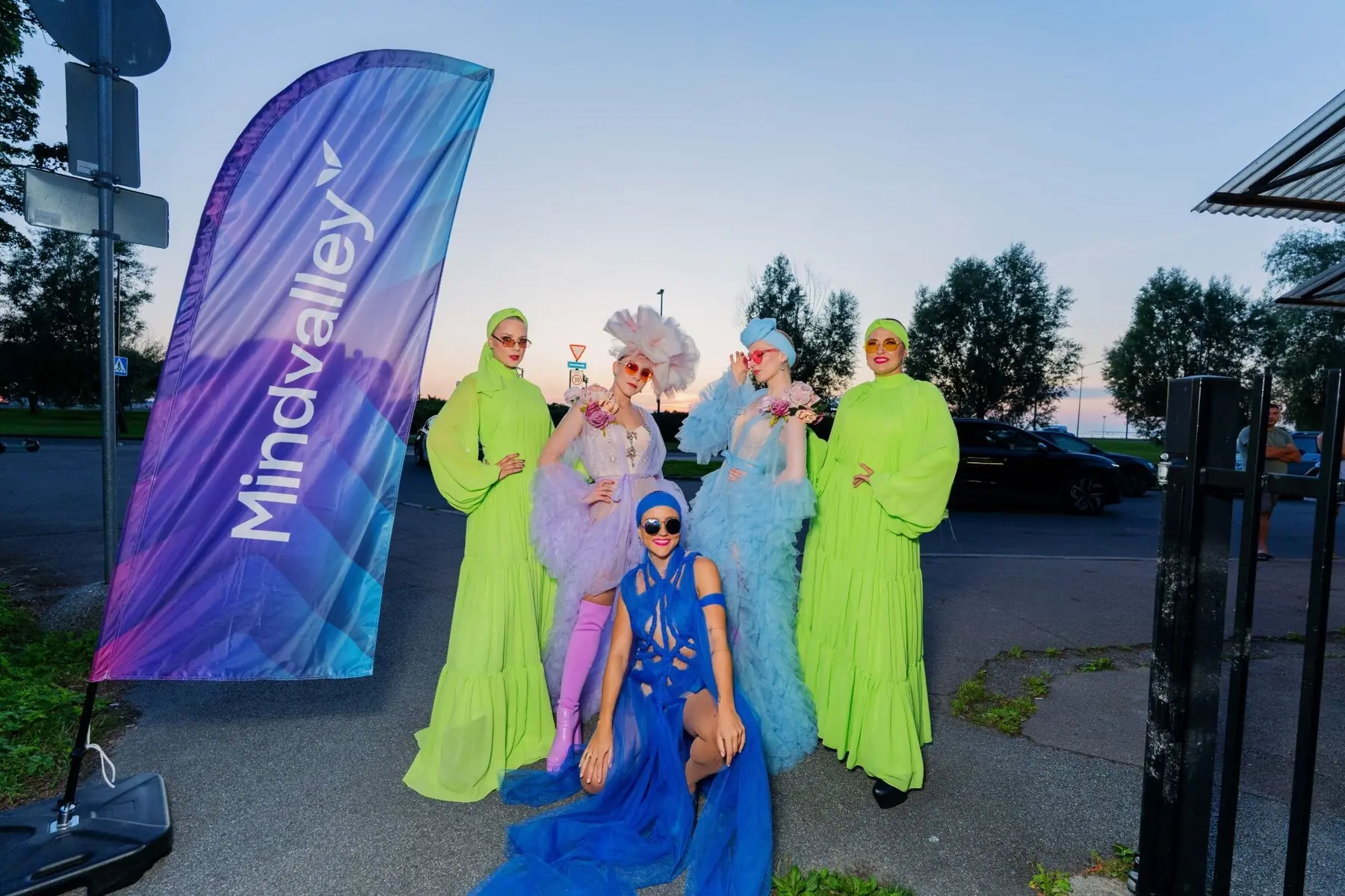 Costumed performers beside a Mindvalley flag at sunset