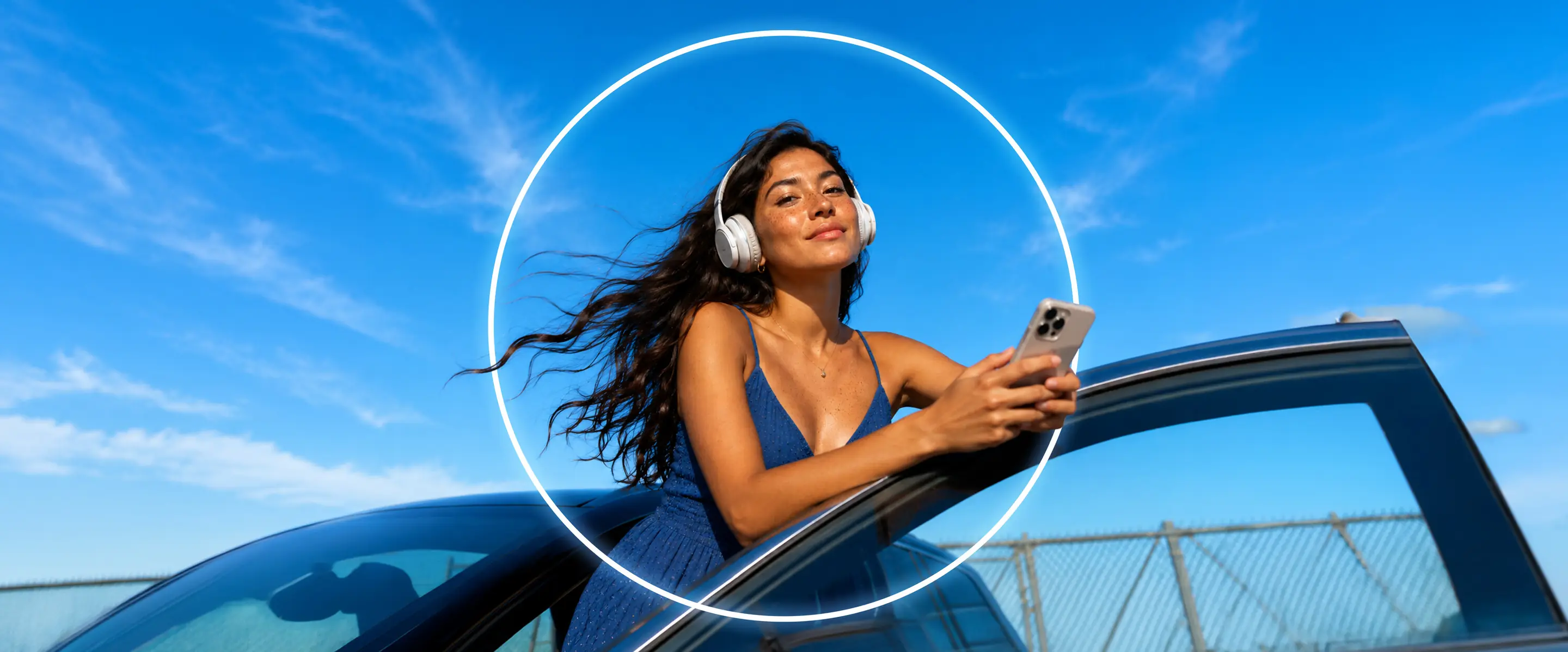 Woman with headphones looking up from a car roof, framed by the Omvana ring