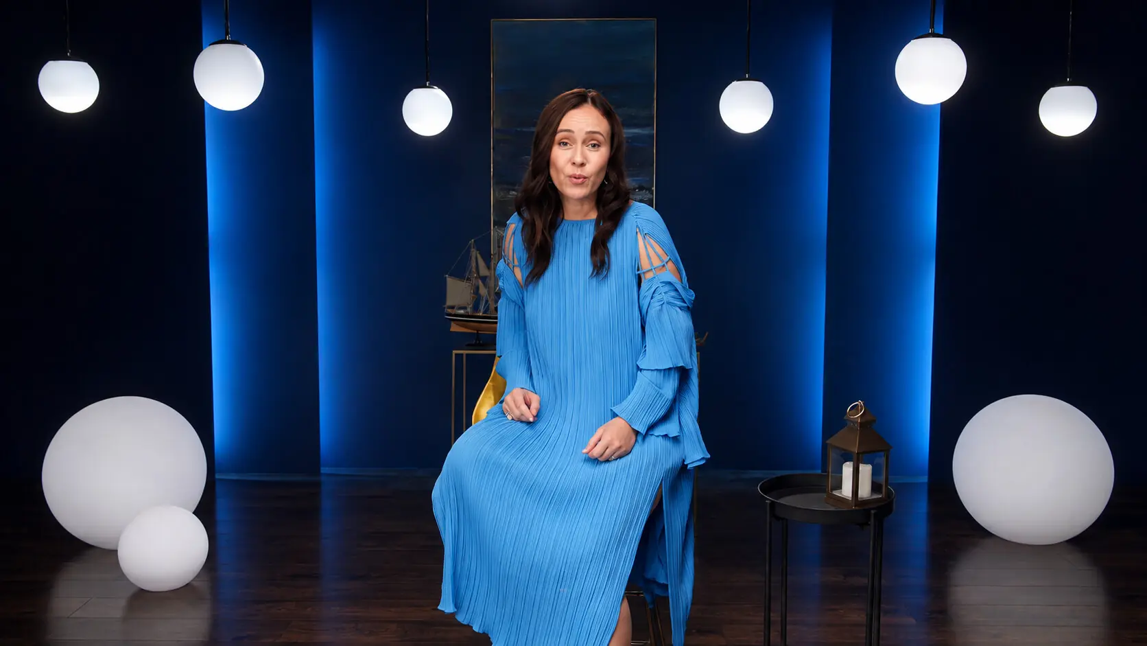 Speaker in a blue dress on a stage of blue light, glowing globes and hanging pendants