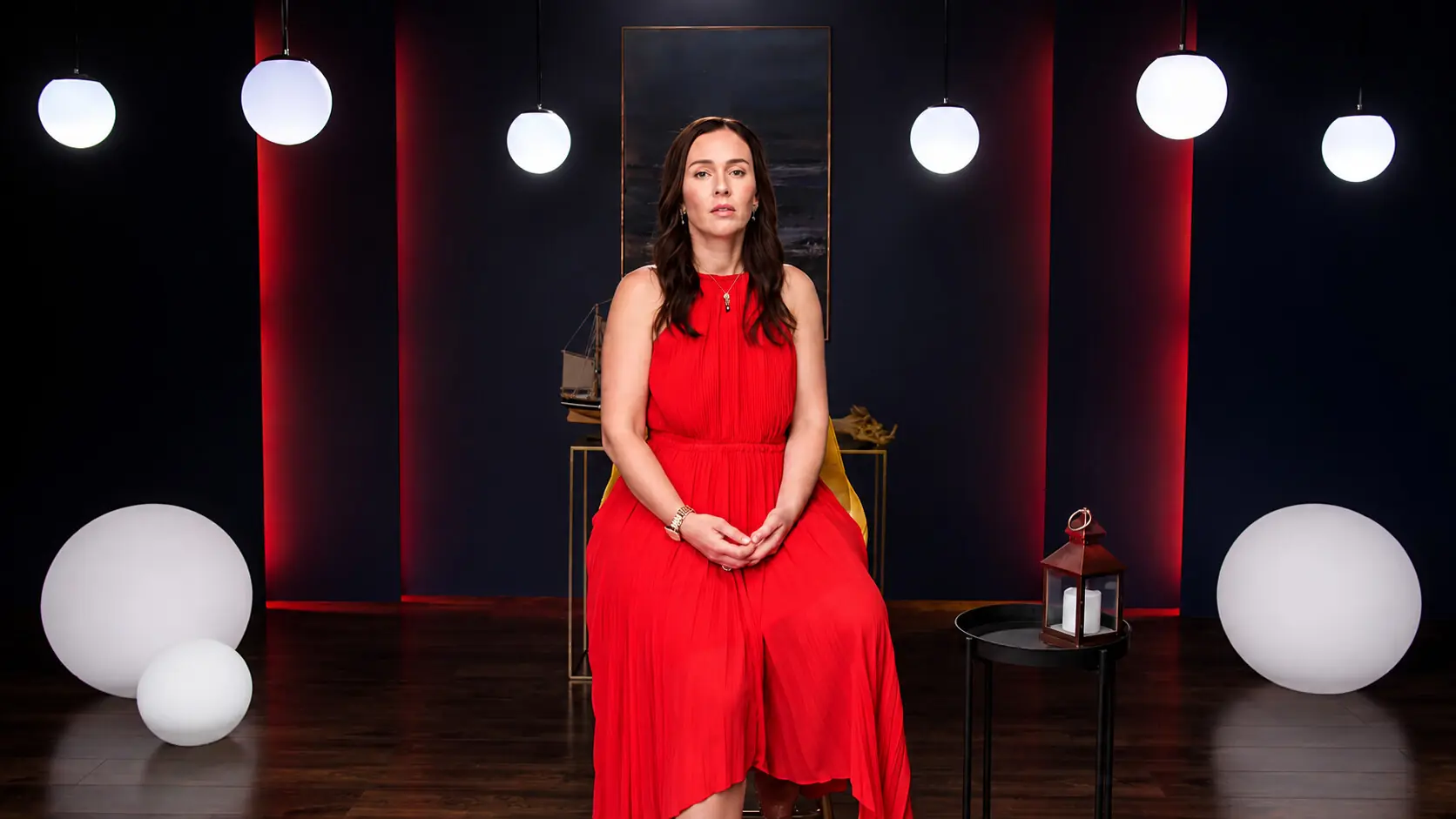 Speaker in a red dress on a red-lit stage with glowing globes